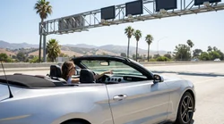 White car rental driving on a bright California highway passing an overhead toll road sign