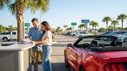 Two people exchanging keys across the front seats of a car rental in sunny Florida