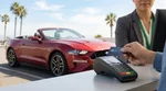 Person tapping a contactless credit card on a payment terminal at a California car hire counter