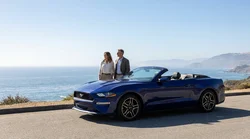Happy couple driving a convertible car rental along a sunny coastal road in California