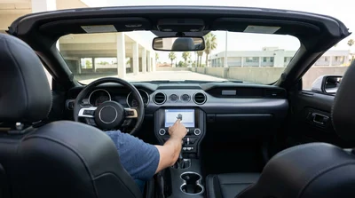 Person touching the digital dashboard screen of a car rental parked on a sunny street in Los Angeles