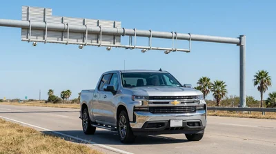 Silver car rental passing under an electronic toll road gantry on a sunny Texas highway