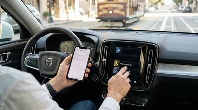 Person holding a smartphone near the dashboard display inside a car rental in San Francisco