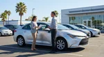 White car rental driving along a scenic coastal road in California under a clear blue sky
