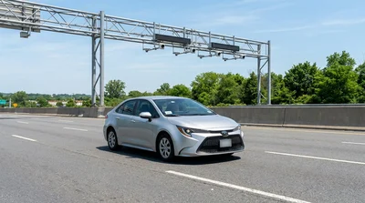 White car rental driving under an electronic toll gantry on a New York highway