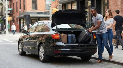 A couple quickly unloading luggage from a black rental car parked curbside on a busy Manhattan street.