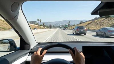 A driver's view from inside a moving rental car on a bright Los Angeles freeway, utilizing the clean HOV lane.