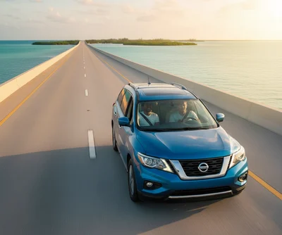 A blue Nissan Pathfinder SUV with two people inside driving on a long, scenic bridge over the ocean with small islands in the distance at sunset, perfect for a Florida Keys road trip with a car rental.