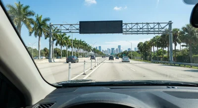 A view from inside a car driving down a busy highway in South Florida, showing the separation between lanes under a blue sky.