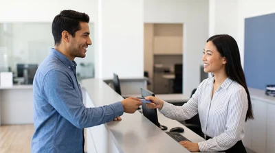 Customer hands card to smiling staff member at a Miami car hire rental counter.