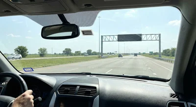 View from the driver's seat inside a rental car, focusing on a toll transponder tag attached to the windshield for use on Texas highways.